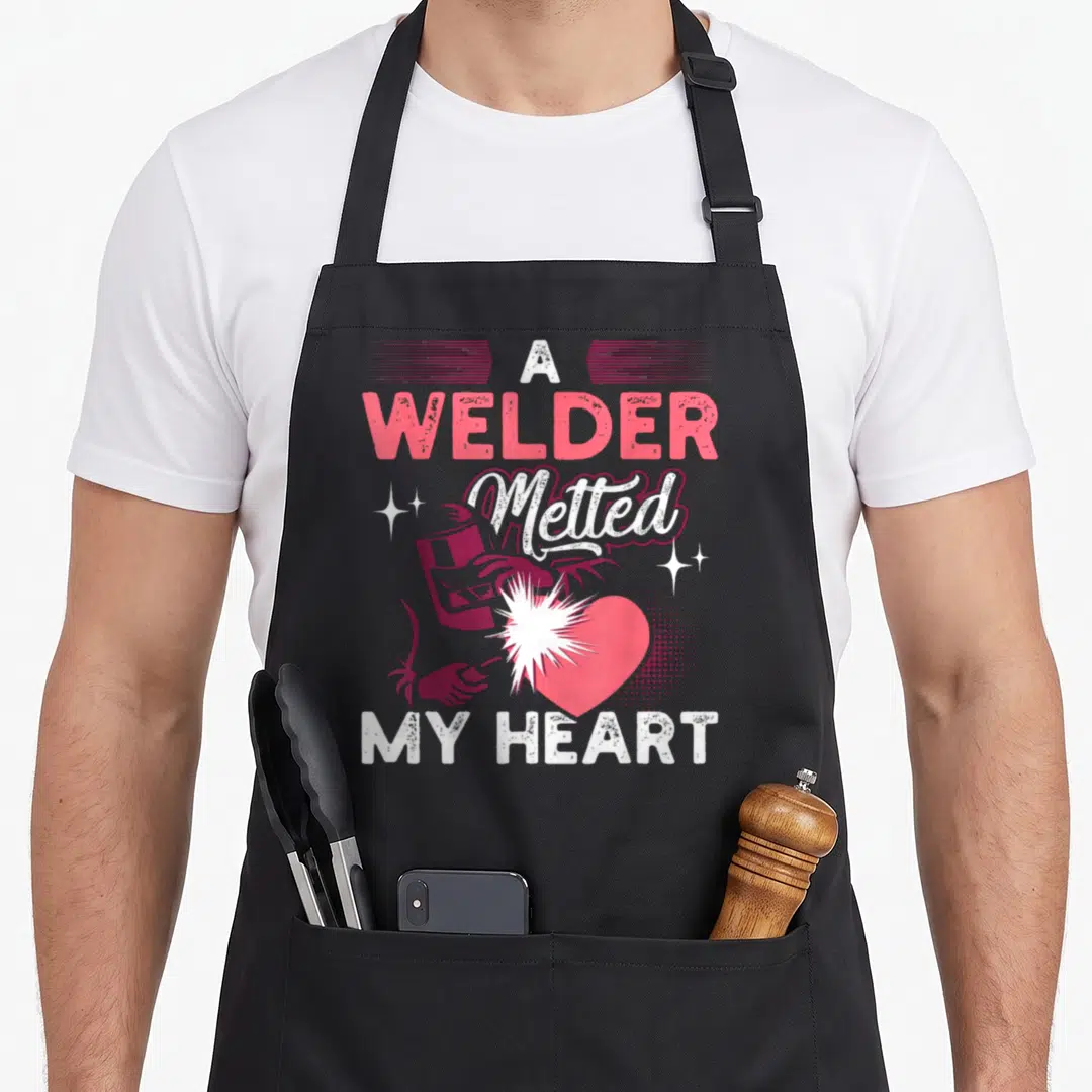Welder wife apron - A Welder Melted My Heart text with pink welder graphic and stars — shown on a black cotton canvas apron against a white background