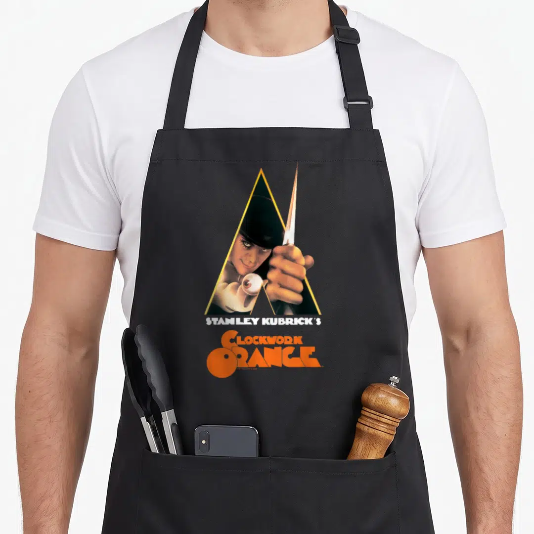 Clockwork novelty apron - Man holding knife in yellow triangle with Stanley Kubrick's Clockwork Orange text — shown on a black cotton canvas apron against a white background