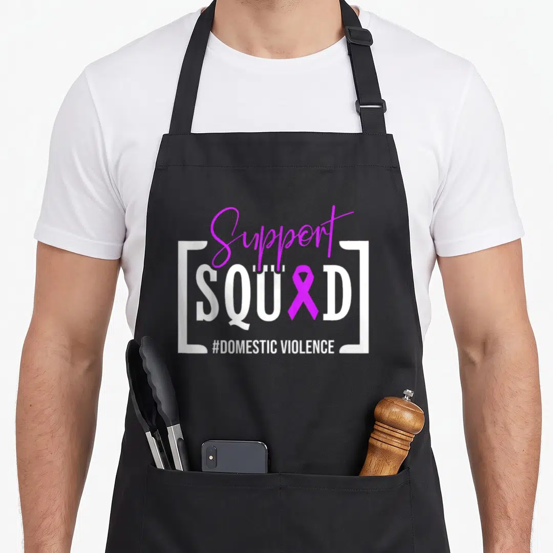 Squad domestic aprons - Purple script Support text over white SQUAD bracketed text with purple ribbon replacing — shown on a black cotton canvas apron against a white background