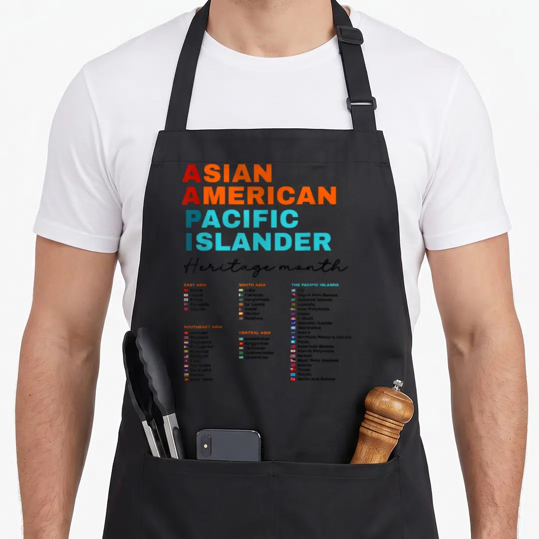 Aapi pacific asian apron - ASIAN AMERICAN PACIFIC ISLANDER text with five regional country lists and flags in red — shown on a black cotton canvas apron against a white background