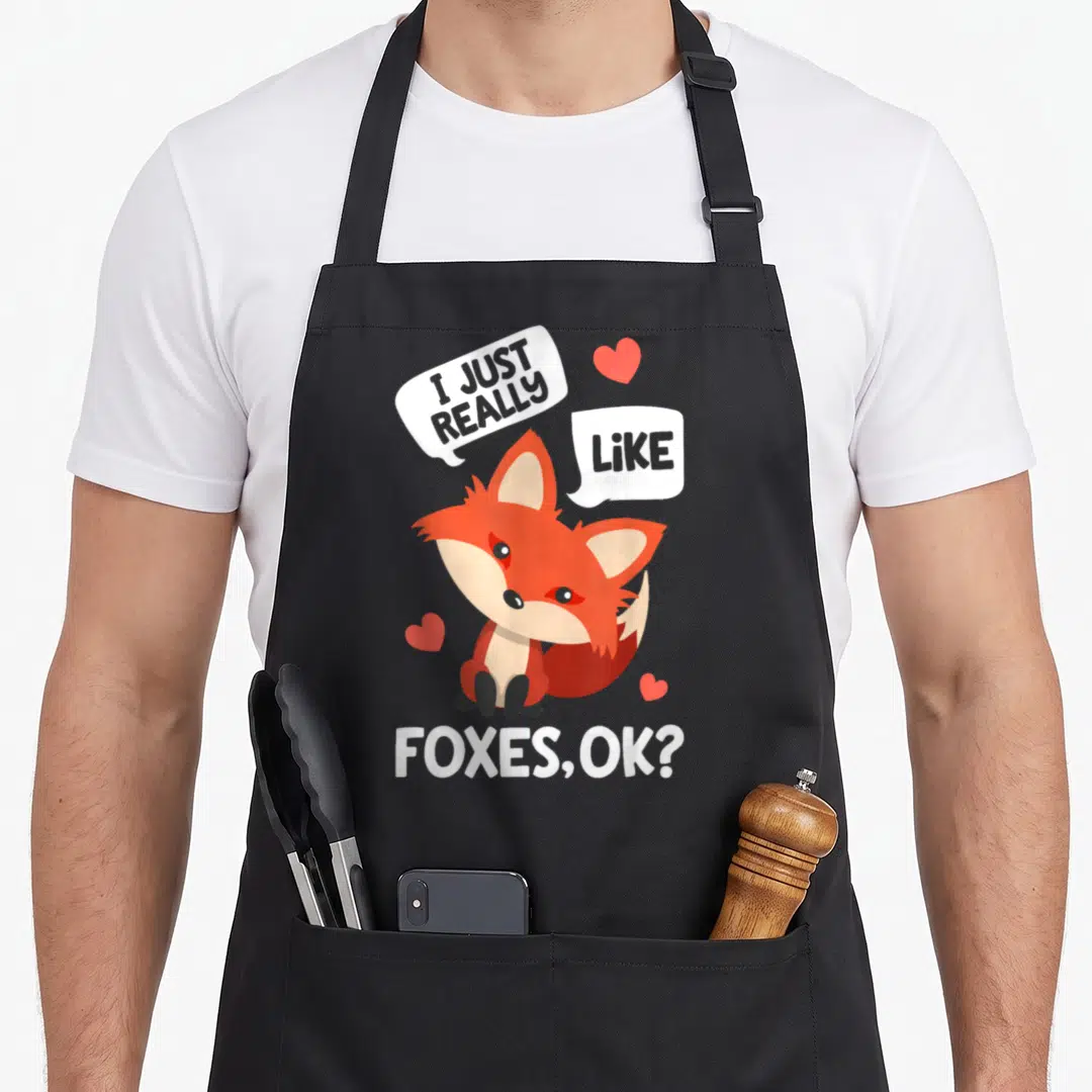 Funny animal fox aprons - Cartoon fox surrounded by hearts and speech bubbles reading I Just Really Like Foxes OK — shown on a black cotton canvas apron against a white background