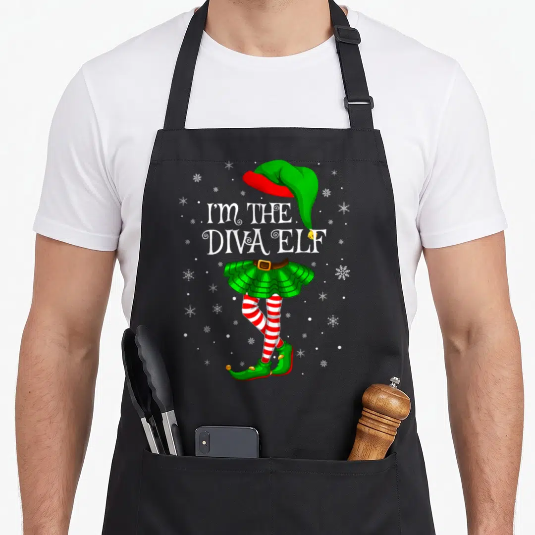 Family diva christmas elf apron - I'M THE DIVA ELF text above green skirt and striped legs with snowflakes — shown on a black cotton canvas apron against a white background