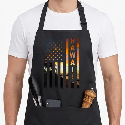 Hawaii american flag apron - USA flag shape filled with Hawaiian sunset photo and vertical HAWAII text in orange — shown on a black cotton canvas apron against a white background