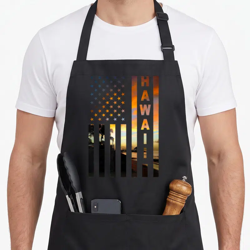 Hawaii american flag apron - USA flag shape filled with Hawaiian sunset photo and vertical HAWAII text in orange — shown on a black cotton canvas apron against a white background