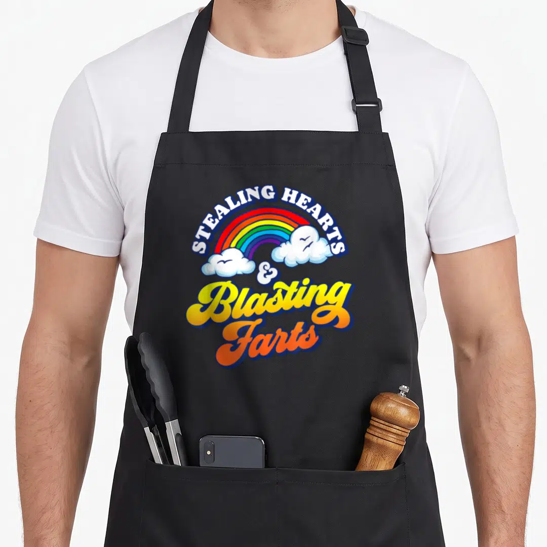 Stealing valentine apron - Rainbow with clouds and STEALING HEARTS Blasting Farts script text — shown on a black cotton canvas apron against a white background