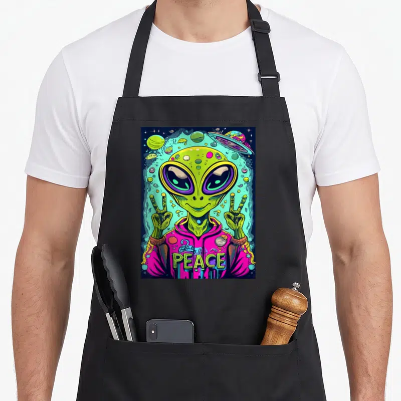 Funny abduction alien ufo apron - Green alien in pink hoodie making double peace signs with planets and UFO — shown on a black cotton canvas apron against a white background