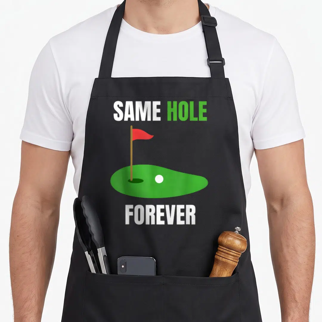 Bachelor wedding apron - Same Hole Forever text above green putting green with red flag and white ball — shown on a black cotton canvas apron against a white background