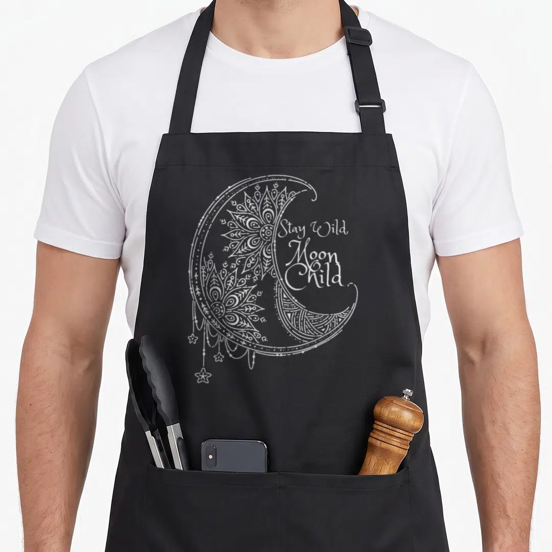 Funny stay moon child apron - White crescent moon with mandala patterns and hanging stars next to stacked text — shown on a black cotton canvas apron against a white background