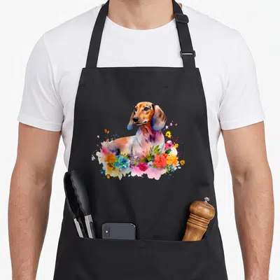 Dachshund top dog aprons - Watercolor dachshund with pink yellow blue green flowers overlapping chest — shown on a black cotton canvas apron against a white background