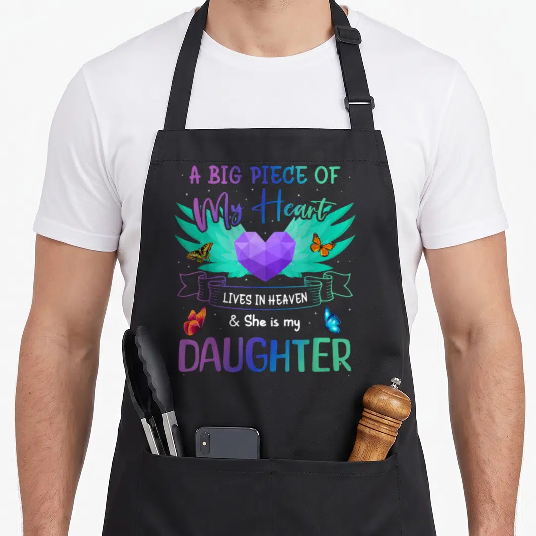 Congratulation angels and aprons - Winged purple heart with butterflies and daughter tribute text in pastel gradient — shown on a black cotton canvas apron against a white background