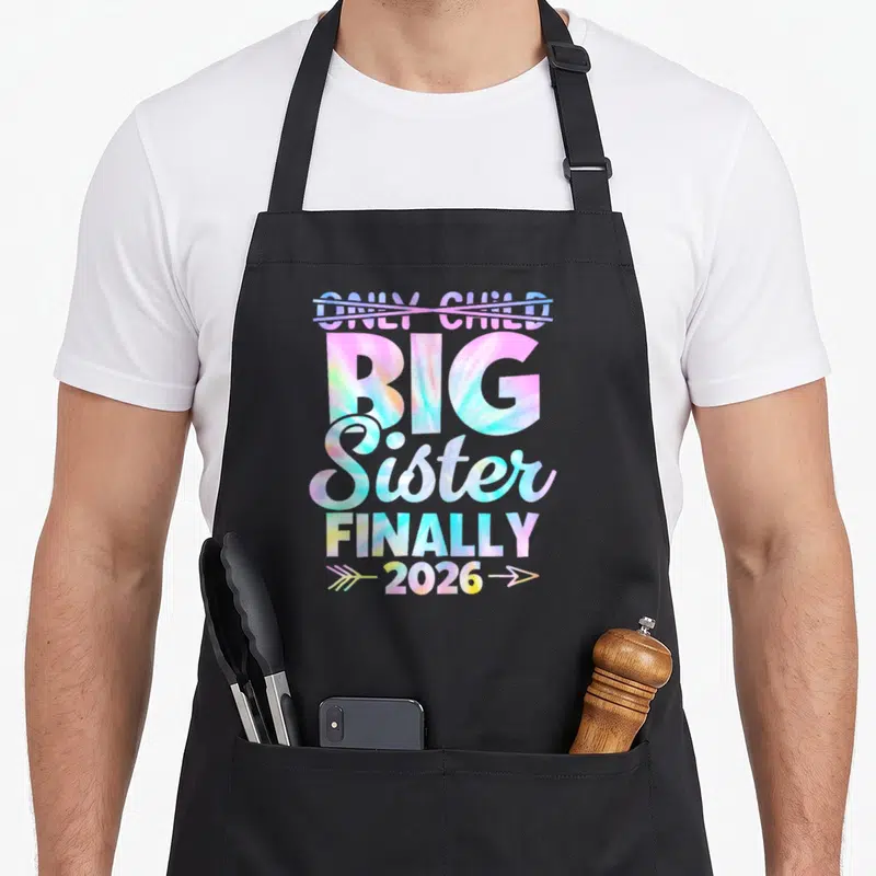 Expire big sister apron - Tie-dye text crossing out ONLY CHILD with BIG Sister finally 2026 arrows — shown on a black cotton canvas apron against a white background