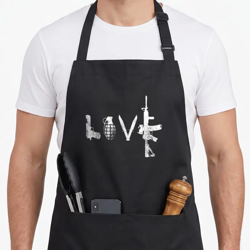 Ar15 gun apron - Four white weapons including pistol grenade and rifle arranged to spell LOVE in distressed style — shown on a black cotton canvas apron against a white background