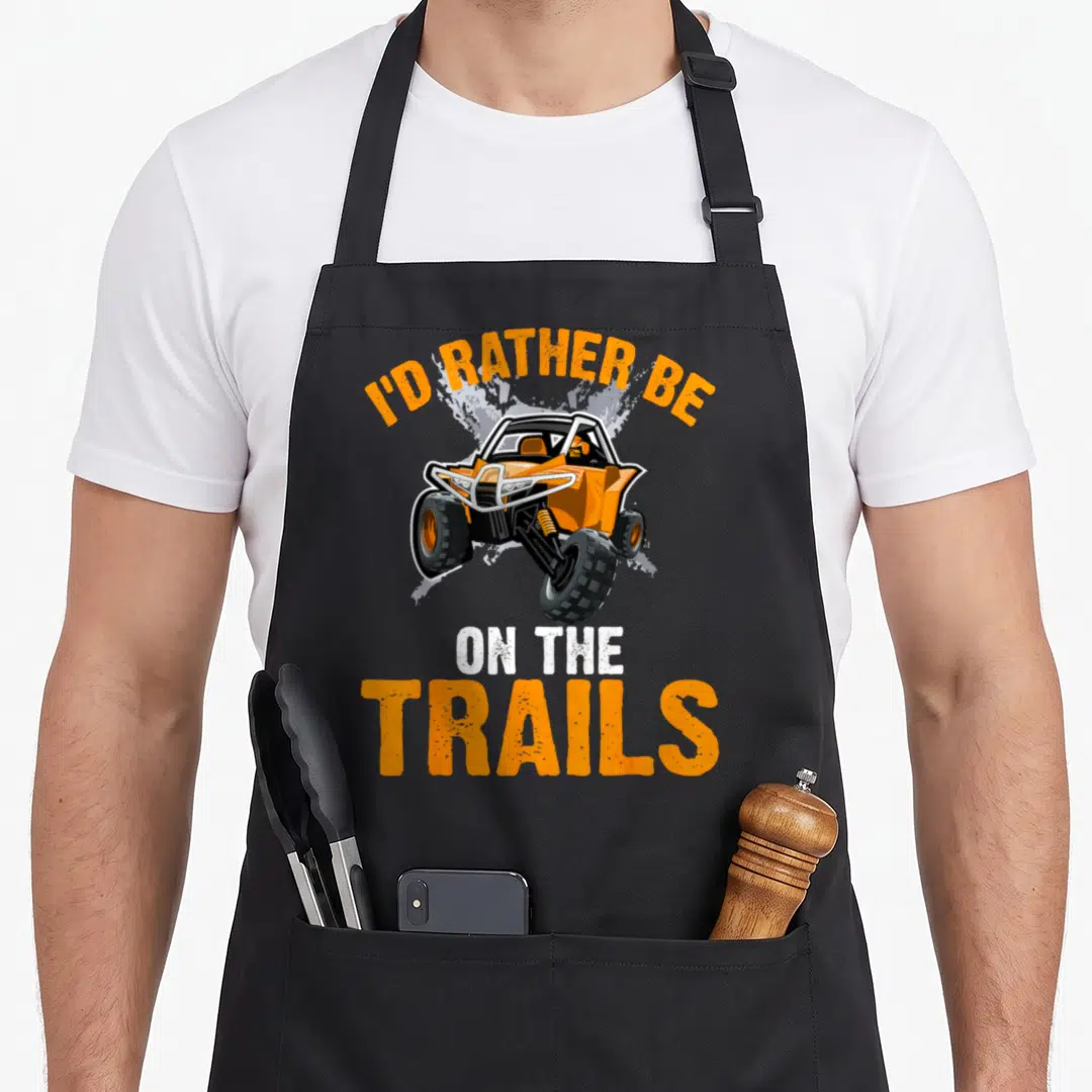 Rather atv apron - Orange cartoon UTV with dirt splash and text I'd Rather Be On The Trails — shown on a black cotton canvas apron against a white background