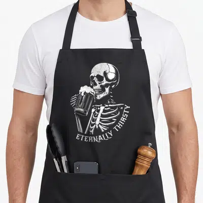 Skeleton craft apron - White distressed skeleton holding foaming beer mug with arched ETERNALLY THIRSTY text — shown on a black cotton canvas apron against a white background