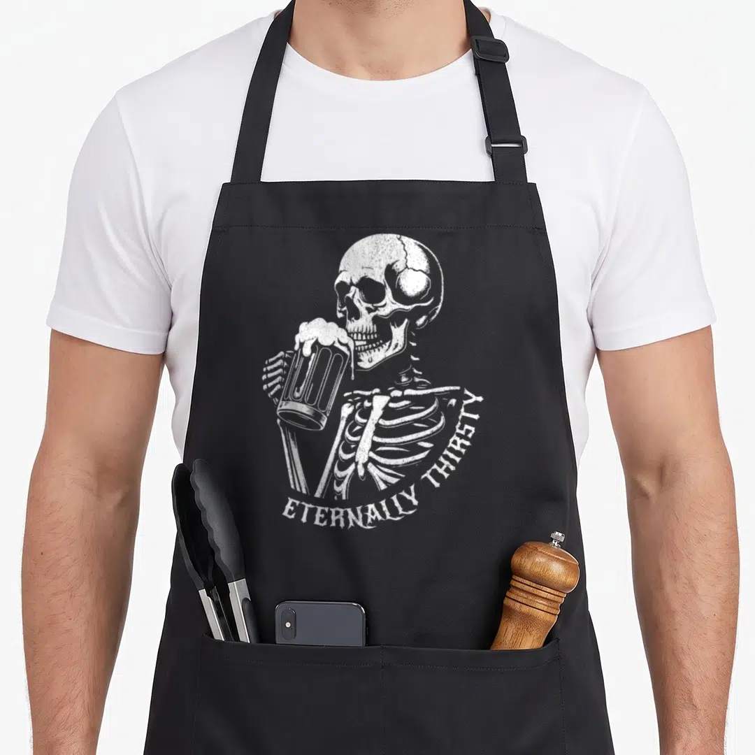 Skeleton craft apron - White distressed skeleton holding foaming beer mug with arched ETERNALLY THIRSTY text — shown on a black cotton canvas apron against a white background