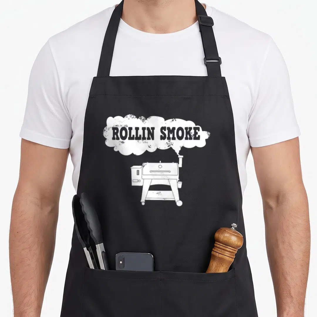 Pellet meat aprons - White ROLLIN SMOKE text in smoke cloud above pellet grill illustration — shown on a black cotton canvas apron against a white background