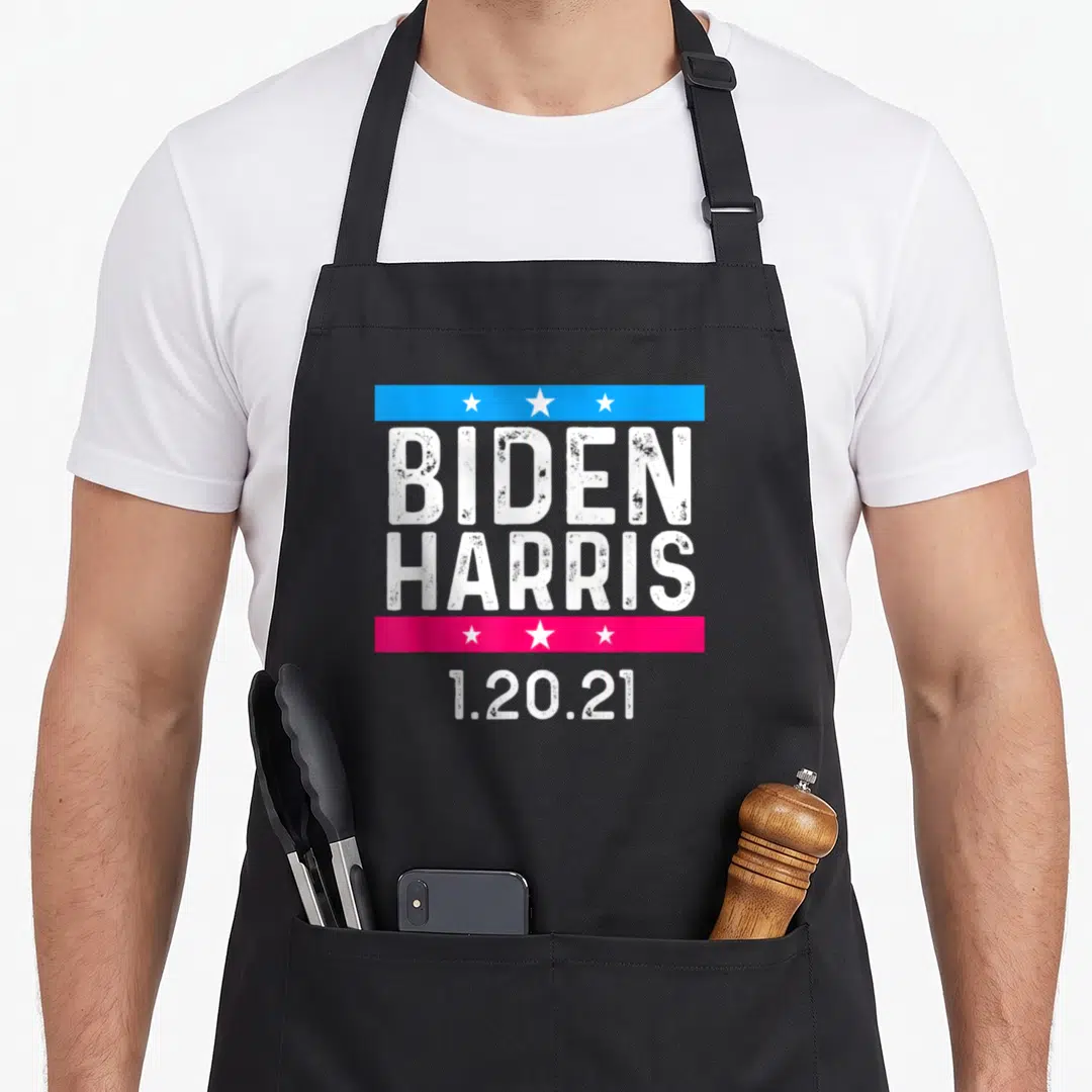 Inauguration date apron - White Biden Harris 1.20.21 text with blue and pink star bars — shown on a black cotton canvas apron against a white background