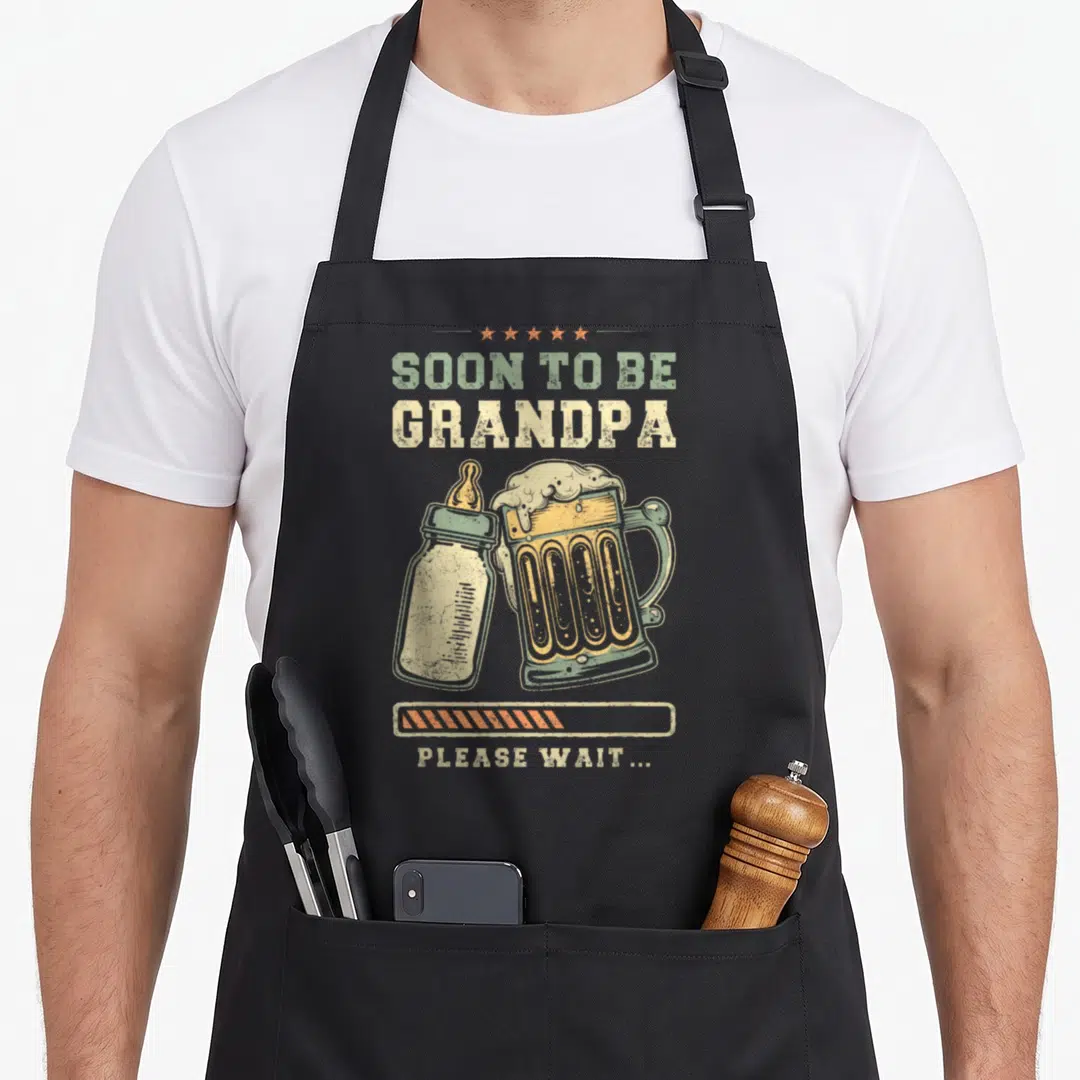 Soon grandpa apron - Retro beer mug and baby bottle with SOON TO BE GRANDPA text and loading bar — shown on a black cotton canvas apron against a white background