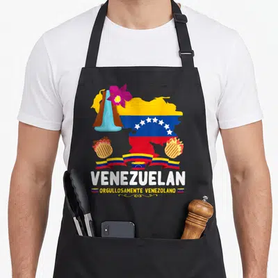 Flag chef outfit with apron - Venezuelan map filled with flag colors, purple orchid, two arepas, and white text — shown on a black cotton canvas apron against a white background