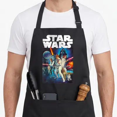 Cast star war apron - STAR WARS text above Luke Skywalker and Darth Vader photo montage in blue and red — shown on a black cotton canvas apron against a white background
