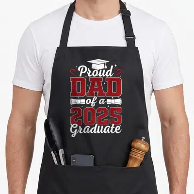 Graduate senior dad apron - Proud DAD of a 2025 Graduate text with cap, diplomas, hearts, and stars in red and white — shown on a black cotton canvas apron against a white background