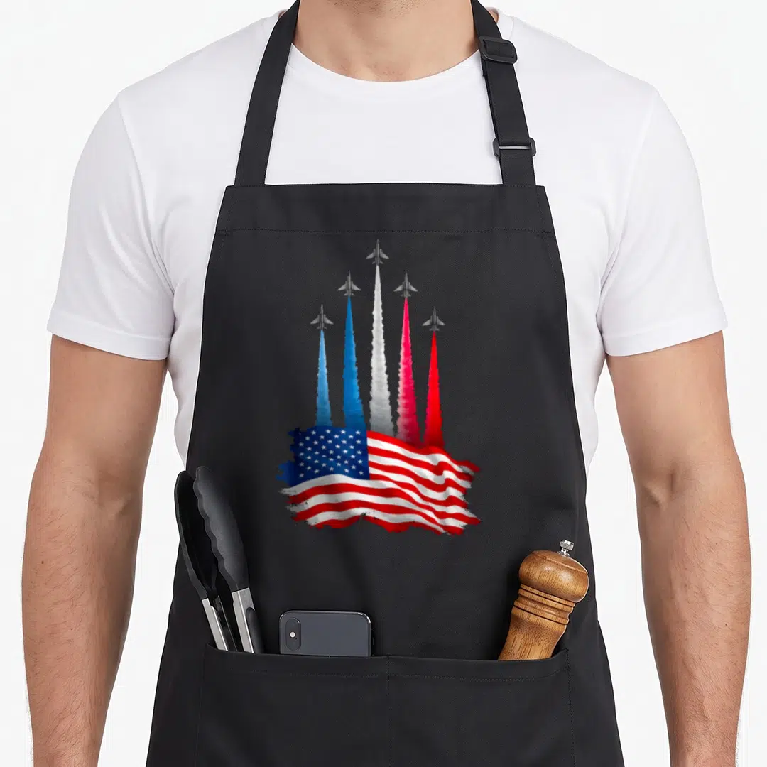 Plane american flag apron - Five grey jets leaving red white blue smoke trails merging into a waving US flag — shown on a black cotton canvas apron against a white background