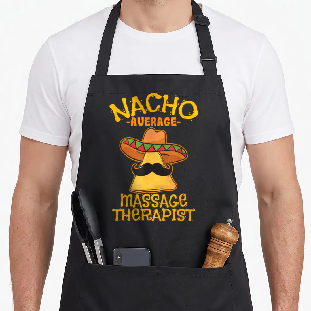 Nacho massage therapist apron - Cartoon nacho chip with sombrero and mustache, text NACHO -AVERAGE- massage THERAPIST — shown on a black cotton canvas apron against a white background