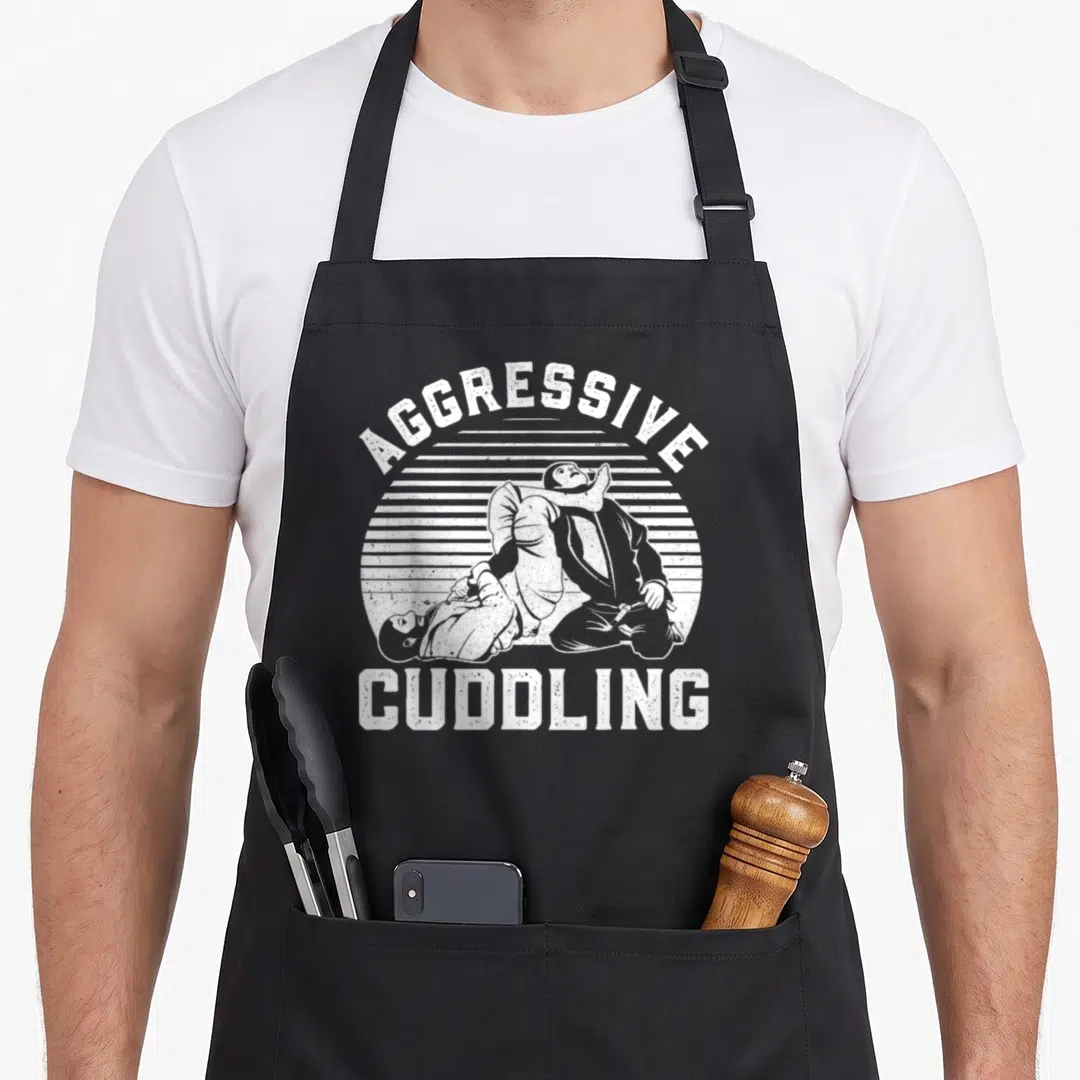 Jiu bjj jitsu apron - White distressed wrestlers with aggressive cuddling text arching over sunburst background — shown on a black cotton canvas apron against a white background