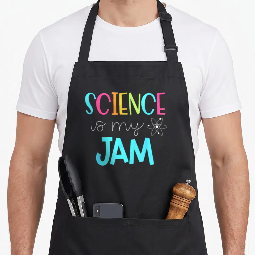 Funny science teacher apron - SCIENCE is my JAM text in blue pink orange green white with atom icon — shown on a black cotton canvas apron against a white background