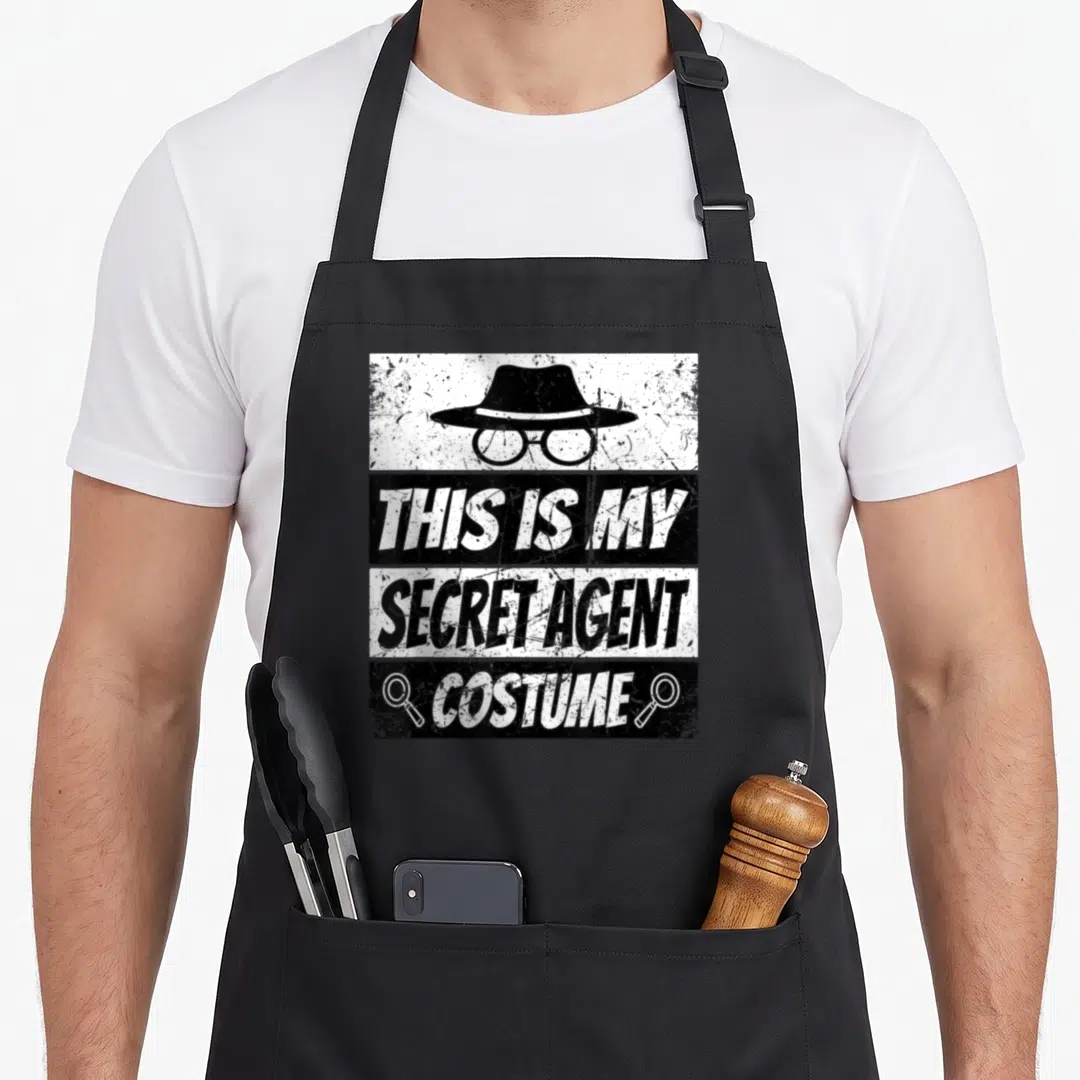 Inspector agent apron - Distressed hat glasses and text reading THIS IS MY SECRET AGENT COSTUME with two magnifying — shown on a black cotton canvas apron against a white background