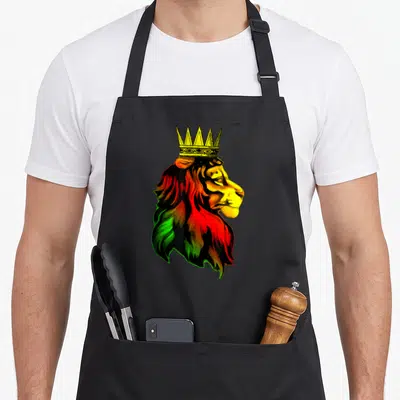 Rastafarian lion apron - Profile lion head wearing a yellow crown with mane in red, green, and black — shown on a black cotton canvas apron against a white background