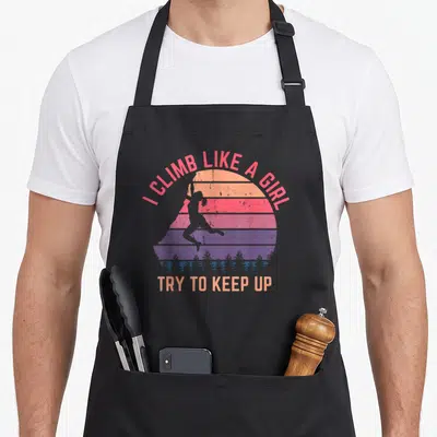 Try climbing apron - Retro sunset with climber silhouette and I climb like a girl text — shown on a black cotton canvas apron against a white background