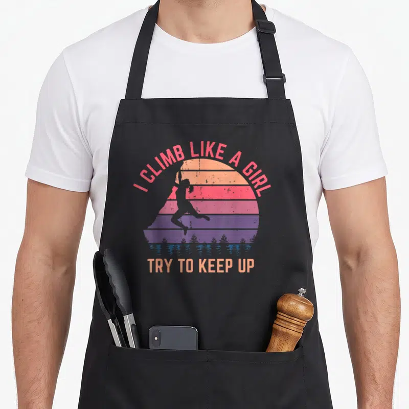 Try climbing apron - Retro sunset with climber silhouette and I climb like a girl text — shown on a black cotton canvas apron against a white background