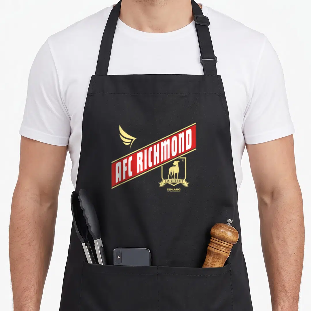 Crossed richmond apron - AFC Richmond red banner gold wing shield dog logo TED LASSO minimalist print — shown on a black cotton canvas apron against a white background