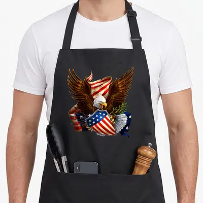 Shield 4th of july apron - Realistic bald eagle holding shield and olive branch with waving flag in brown red white blue — shown on a black cotton canvas apron against a white background