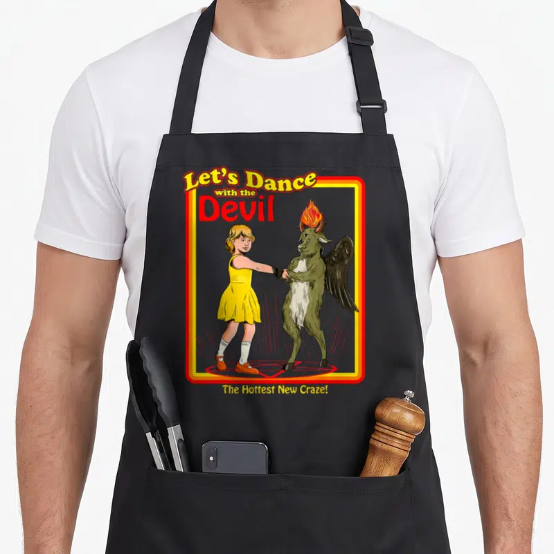 Witchcraft devil's apron - Cartoon girl in yellow dress dancing with a horned devil on a red pentagram surrounded — shown on a black cotton canvas apron against a white background
