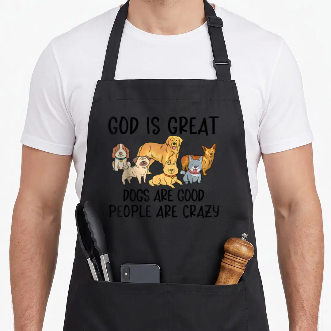 Vintage god cooking with dog apron - Six cartoon dogs below black text reading GOD IS GREAT DOGS ARE GOOD PEOPLE ARE — shown on a black cotton canvas apron against a white background