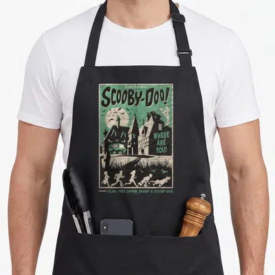Mystery movie poster apron - Retro poster art with Scooby-Doo gang running past spooky houses in green and black — shown on a black cotton canvas apron against a white background