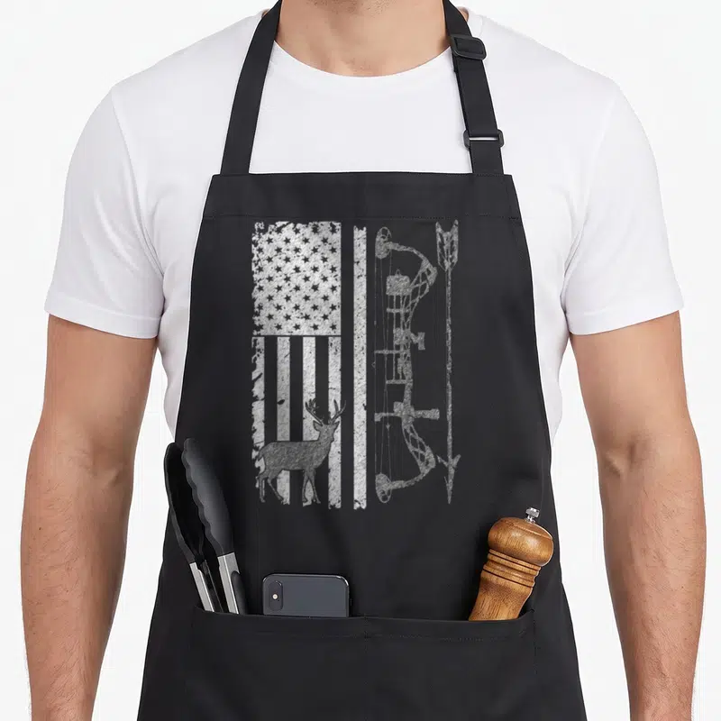Hunting grill hunter apron - Distressed white USA flag, deer silhouette, and vertical bow printed on black fabric — shown on a black cotton canvas apron against a white background