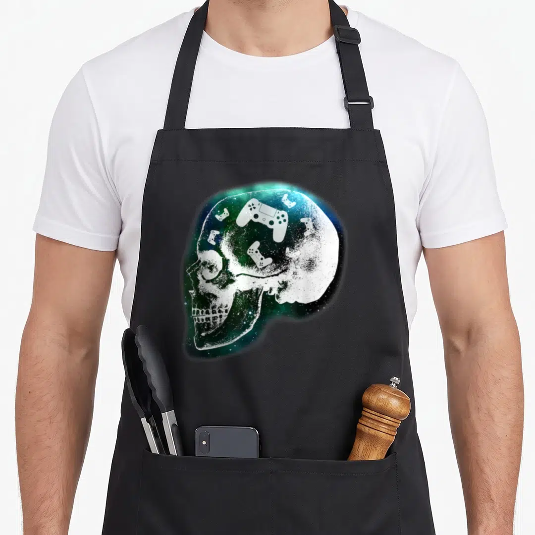 Mind gaming apron - Realistic white skull in profile filled with blue green galaxy and scattered game controllers — shown on a black cotton canvas apron against a white background