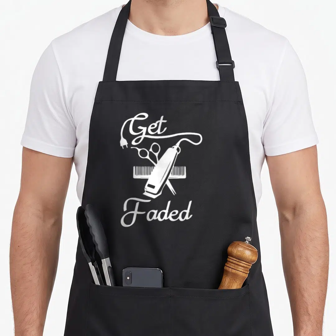 Faded haircut apron - White line art of hair clipper, scissors, comb and Get Faded text — shown on a black cotton canvas apron against a white background