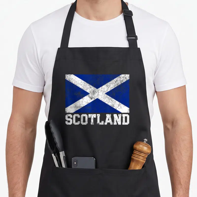 Scottish family aprons - Distressed blue and white saltire flag with SCOTLAND text below — shown on a black cotton canvas apron against a white background