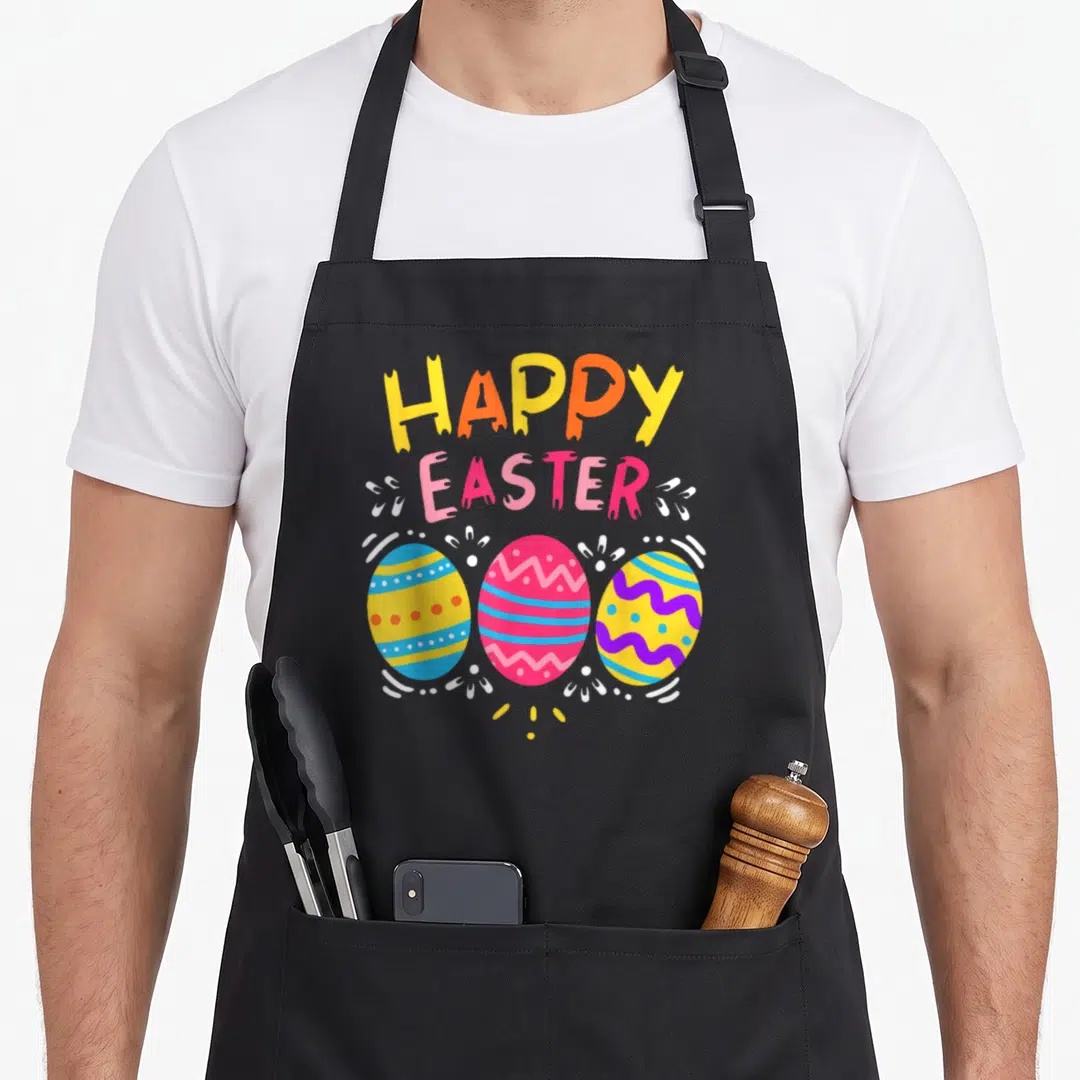 Colorful easter egg apron - HAPPY EASTER text above three yellow, pink, blue, and purple decorated eggs with white — shown on a black cotton canvas apron against a white background