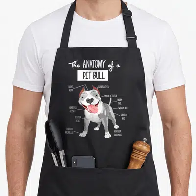 Pitbull anatomy apron - Cartoon pit bull diagram with labels like snack detector and golden heart pointing to body parts — shown on a black cotton canvas apron against a white background