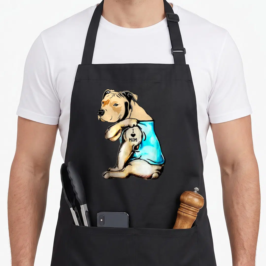 Pit tattoo apron - Tan dog in blue shirt with I heart MOM tattoo text on arm — shown on a black cotton canvas apron against a white background