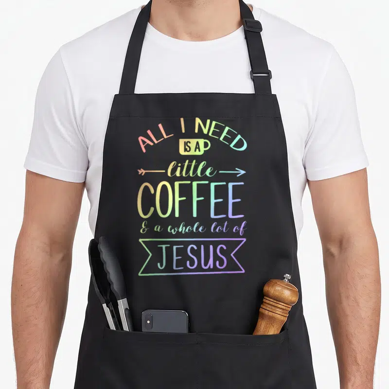 Whole lot coffee apron - Rainbow stacked text reading All I Need Is A Little Coffee And A Whole Lot Of Jesus with cup — shown on a black cotton canvas apron against a white background