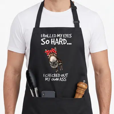 Rolled optics apron - Cartoon donkey with red polka dot bandana and sarcastic text quote — shown on a black cotton canvas apron against a white background