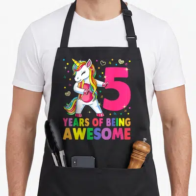 Flossing birthday apron - Cartoon unicorn flossing next to pink number 5 and rainbow text YEARS OF BEING AWESOME — shown on a black cotton canvas apron against a white background