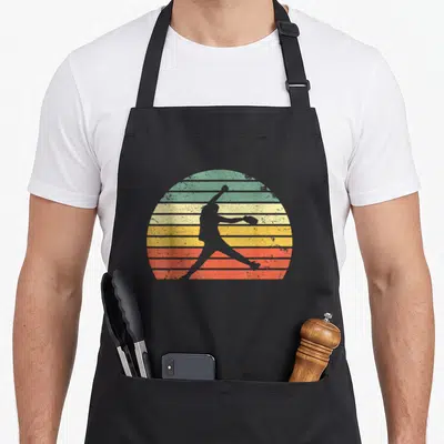 Pitching softball apron - Grey softball pitcher silhouette against retro striped sun in green yellow orange red — shown on a black cotton canvas apron against a white background