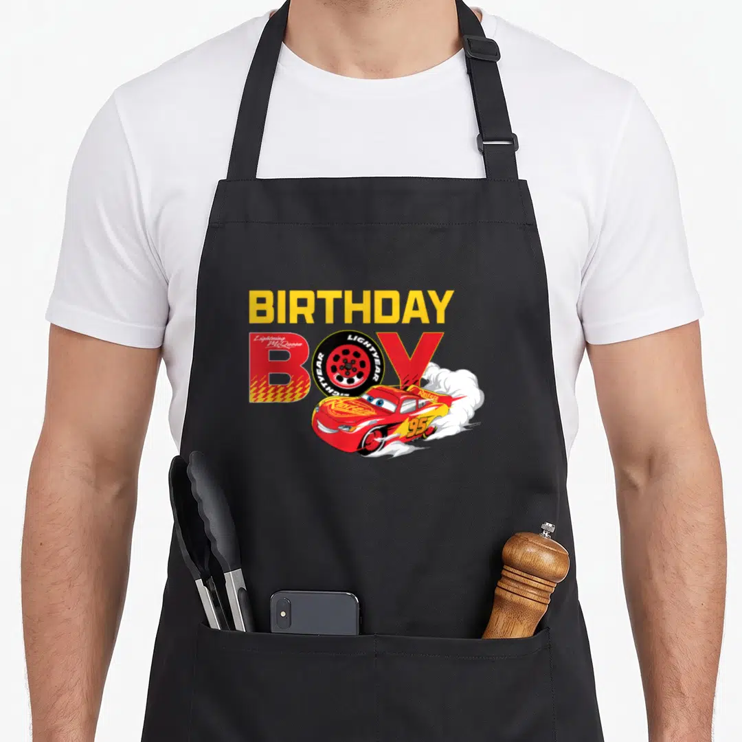 Funny birthday car apron - Red race car with BIRTHDAY BOY text where O is a tire and white smoke trails behind — shown on a black cotton canvas apron against a white background
